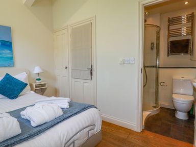 A bedroom with a bed a side table with lamp and an ensuite bathroom at Periwinkle Atlantic Highway near Bude