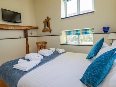 A bedroom with a bed with blue pillows white towels a wooden chair and a wall-mounted TV at Periwinkle Atlantic Highway near Bude