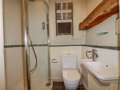 A bathroom with a corner shower unit a toilet a sink a towel rail and a wooden beam at Periwinkle Atlantic Highway near Bude