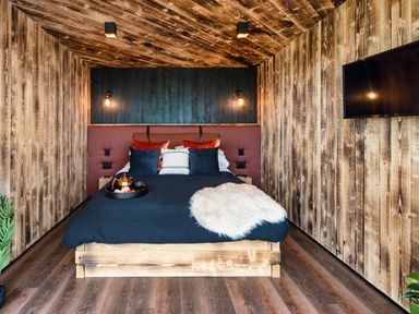 A bedroom with a wooden bed frame and walls with cushions pillows and a television mounted on the wall at Rusty Boathouse in Llanarth