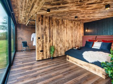 A bedroom with a wooden bed and blue bedding beside large glass windows at Rusty Boathouse in Llanarth