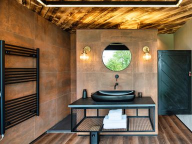 A bathroom with a black sink on a metal stand with towels on the shelf and a round mirror above at Rusty Boathouse in Llanarth