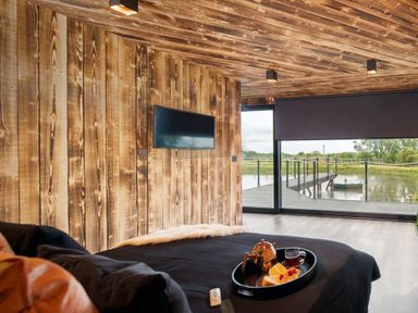 A bedroom with wooden walls and ceiling a wall-mounted TV and a window with a view of a dock and water at Rusty Boathouse in Llanarth