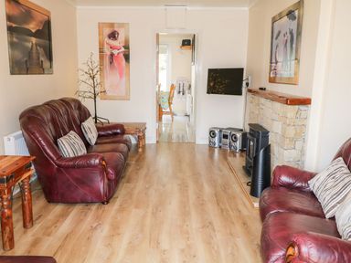 A living room with two brown leather sofas a wooden side table a wall-mounted television and a stereo system at Bridgetown Cottage in Kerrykeel County Donegal