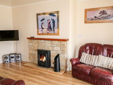 A living room with a leather sofa a fireplace with a fire a television and stereo system at Bridgetown Cottage in Kerrykeel County Donegal