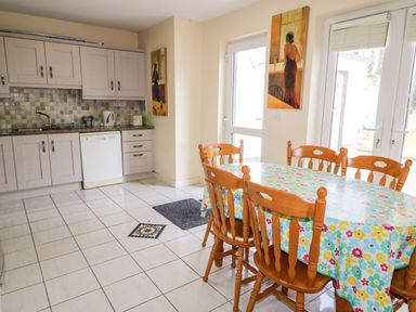 A kitchen with wooden chairs around a table covered with a floral tablecloth and white cabinets at Bridgetown Cottage in Kerrykeel County Donegal