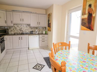 A kitchen with white cabinets a dishwasher a round table with a floral tablecloth and wooden chairs at Bridgetown Cottage in Kerrykeel County Donegal