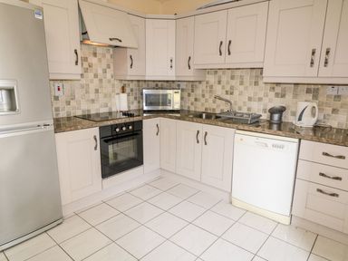 A kitchen with white cabinets stainless steel appliances a microwave oven a sink and a dishwasher at Bridgetown Cottage in Kerrykeel County Donegal