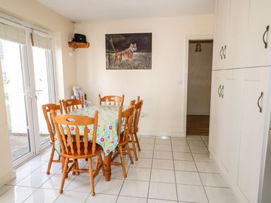 A dining area with a wooden table and six chairs covered with a floral tablecloth next to sliding glass doors and white cabinets at Bridgetown Cottage Kerrykeel County Donegal