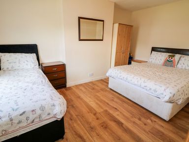 A bedroom with two beds a wooden floor a wardrobe and a mirror on the wall at Bridgetown Cottage in Kerrykeel County Donegal