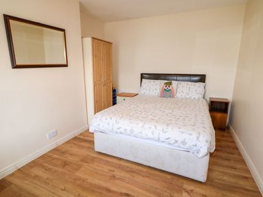 A bedroom with a double bed with patterned bedding a wardrobe two bedside tables and a wall mirror at Bridgetown Cottage in Kerrykeel County Donegal