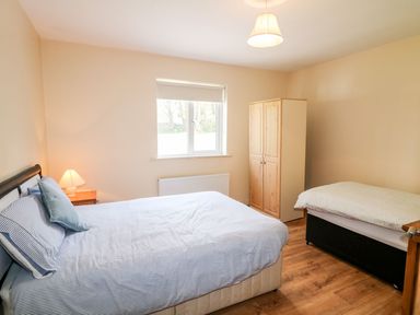 A bedroom with two beds a wooden wardrobe a bedside table with lamp and a window at Bridgetown Cottage in Kerrykeel County Donegal