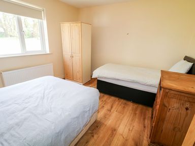 A bedroom with a bed a single bed a wooden wardrobe and a wooden chest of drawers at Bridgetown Cottage in Kerrykeel County Donegal