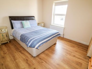 A bedroom with a double bed with blue striped bedding two bedside tables and a window at Bridgetown Cottage in Kerrykeel County Donegal