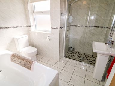A bathroom with a bathtub a toilet a shower with glass doors and a sink at Bridgetown Cottage in Kerrykeel County Donegal