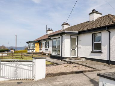 A white single-story house with a brown tiled roof a white front door and a fenced lawn at Bridgetown Cottage in Kerrykeel County Donegal