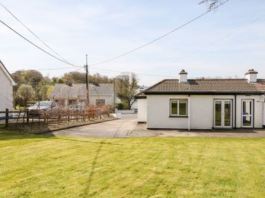 An outdoor view of white houses with tiled roofs and chimneys a concrete driveway a grassy lawn and trees at Bridgetown Cottage in Kerrykeel County Donegal