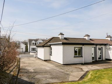 A driveway leading to a white bungalow with a tiled roof and a small grassy area at Bridgetown Cottage in Kerrykeel County Donegal