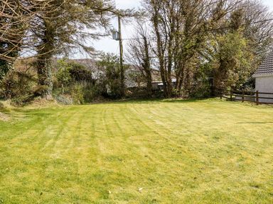 A grassy lawn with trees and a wooden fence next to a building at Bridgetown Cottage in Kerrykeel County Donegal