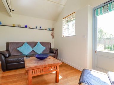 A living room with a brown leather sofa with blue cushions a wooden table with a blue bowl and a glass door at Cameo Atlantic Highway near Bude