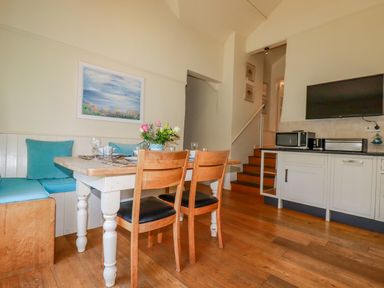 A dining area with a wooden table and chairs a built-in bench with blue cushions a TV microwave and toaster on a counter at Cameo Atlantic Highway near Bude