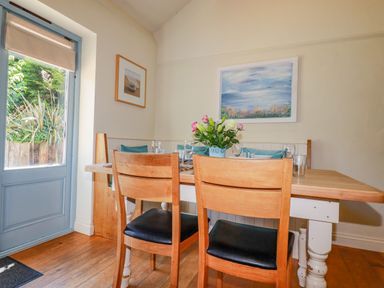 A dining room with a wooden table two wooden chairs and flower vase by a window at Cameo Atlantic Highway near Bude