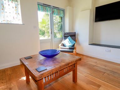 A room with wooden floor a wooden table with a blue bowl a chair with a cushion and glass doors at Cameo Atlantic Highway near Bude