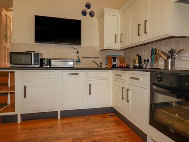 A kitchen with white cabinets countertop appliances and a wall-mounted television at Cameo Atlantic Highway near Bude