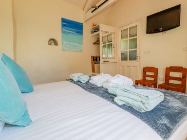A bedroom with folded towels and robes on a bed two wooden chairs a wall-mounted TV and a closet with a mirror at Cameo Atlantic Highway near Bude