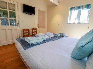 A bedroom with a bed with towels and bathrobes on it two wooden chairs a wall-mounted TV and a window with a striped blind at Cameo Atlantic Highway near Bude