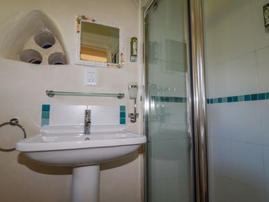 A bathroom with a pedestal sink a mirror a glass shelf and a shower with a glass door at Cameo Atlantic Highway near Bude