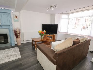 A living room with a sofa facing a television and a wooden coffee table with flowers at Penrallt in Cemaes Bay