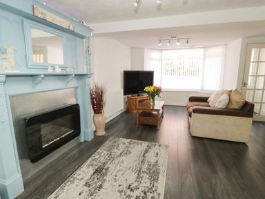 A living room with a fireplace a TV on a stand a sofa and a coffee table with flowers at Penrallt in Cemaes Bay