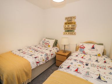 A bedroom with two single beds with nautical themed bedding a wooden nightstand with a lamp and a wall sign above the radiator at Penrallt in Cemaes Bay