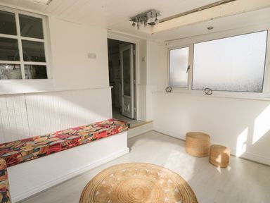 A sitting area with a built-in bench with patterned cushions two round wicker stools and a round woven rug at Penrallt in Cemaes Bay