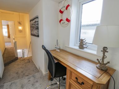 A hallway with a wooden desk chair lamp and nautical decorations at Penrallt in Cemaes Bay