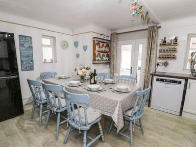 A dining area with a table set for six with blue chairs and kitchen appliances at Penrallt in Cemaes Bay