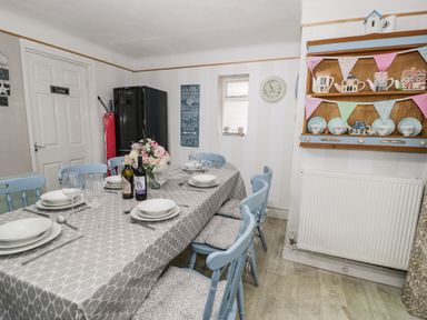 A dining room with a table set for six with dishes and wine bottles and blue chairs at Penrallt in Cemaes Bay