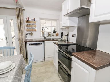 A kitchen with a stove dishwasher sink and dining table with blue chairs at Penrallt in Cemaes Bay