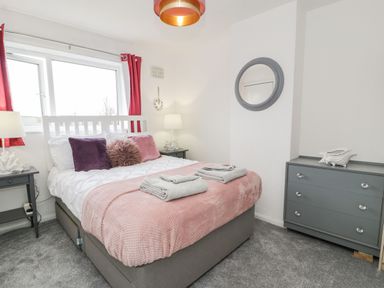 A bedroom with a bed with pink and purple pillows and two grey nightstands with lamps at Penrallt in Cemaes Bay