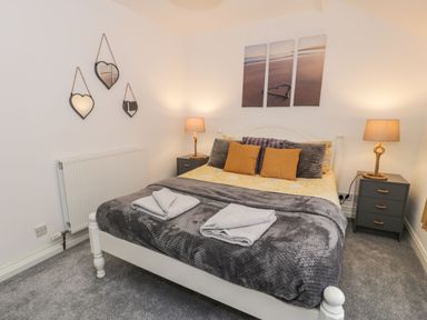 A bedroom with a bed with yellow and gray bedding two bedside tables with lamps and heart-shaped mirrors on the wall at Penrallt in Cemaes Bay