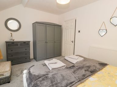 A bedroom with a gray wardrobe a gray chest of drawers a bed with towels on a gray blanket and heart shaped mirrors on the wall at Penrallt in Cemaes Bay