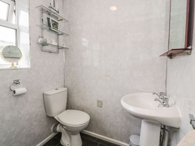 A bathroom with a toilet a pedestal sink glass shelves and a window at Penrallt in Cemaes Bay
