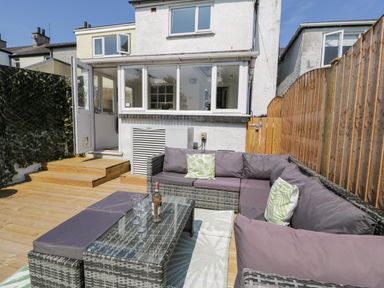 An outdoor patio with wicker sectional sofa and glass table with wine bottle and glasses at Penrallt in Cemaes Bay