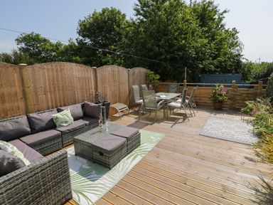 An outdoor wooden deck with lounge seating and a dining table with chairs at Penrallt in Cemaes Bay