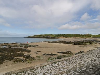 A sandy beach with seaweed and rocks beside a stone pavement at Penrallt in Cemaes Bay