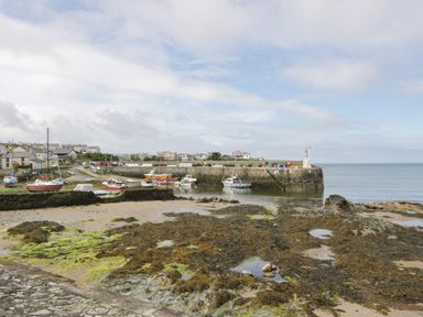 A harbor with boats docked near a stone pier and houses in the background at Penrallt in Cemaes Bay