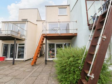The rear view of a modern house with glass balconies wooden stairs and a bush in front at The Moorings in Porthmadog