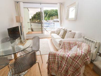 A living room with chairs a glass table a white sofa and a sliding glass door overlooking water at The Moorings in Porthmadog