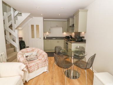 A kitchen with green cabinets a glass dining table with four chairs next to a staircase and an armchair at The Moorings in Porthmadog